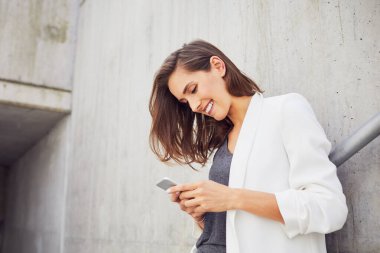 Kendine güveni tam ve neşeli bir kadın dışarıda beton duvara yaslanırken mesaj atıyor.