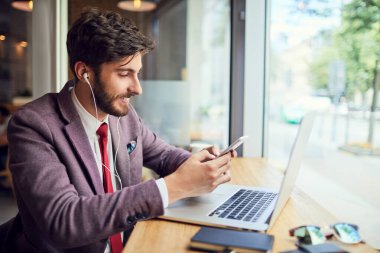 Laptop ve cep telefonu kullanan zarif genç bir işadamı.