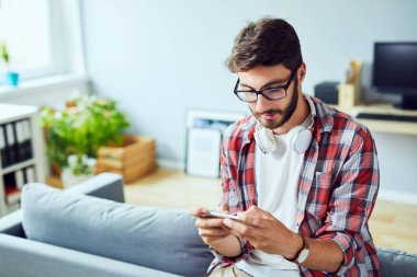 Genç adam evde cep telefonuyla oyun oynuyor.