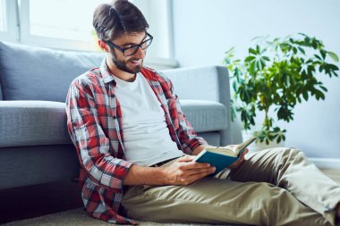 Yerde oturmuş kitap okuyan gülümseyen genç adamın gizli bir fotoğrafı.