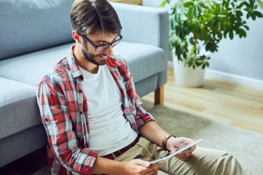 Rahat genç adam yerde oturup tabletten film izliyor.