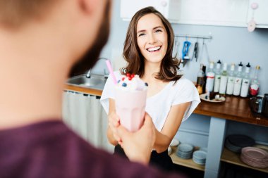 Gülümseyen kadın modern kafede müşteriye milkshake veriyor.