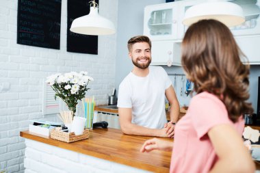 Tezgahın arkasında durup kadın müşterilerden emir alan neşeli bir barmen. 