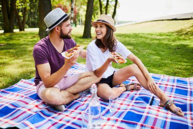 Genç bir çift pikniğe çıkıp birlikte yemek yiyor ve gülüyor. 