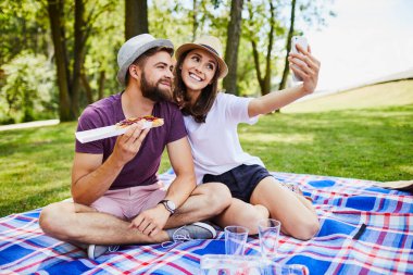 Genç çift parkta piknik yaparken selfie çekiyor.