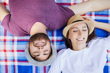 Gülümseyen genç çift, kapalı gözlerle battaniyeye uzanıp dinleniyorlar.