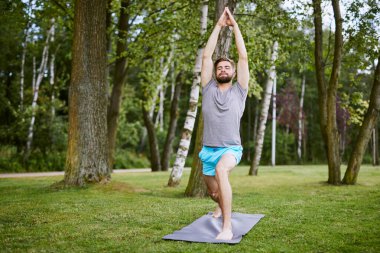 Odaklanmış genç bir adam sabah parkta yoga pozu veriyor.