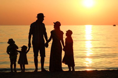 Gün batımı kavramında deniz kenarında bir siluet ailesi.