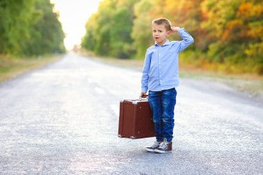 Parka giderken yolda bavulu olan mutlu çocuk.