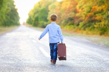 Parka giderken yolda bavulu olan mutlu çocuk.