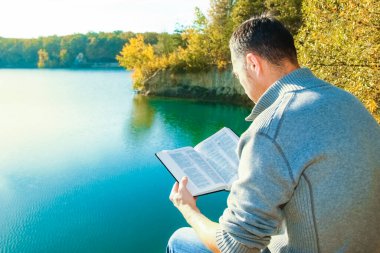 Happy guy reading a book in the park on nature travel education clipart