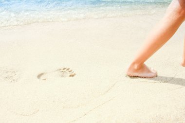 Plaj seyahati. Kumlu bir sahilde yürürken kumların üzerinde ayak izleri bırakan bir kadın. Yunanistan 'da bir plajda altın kumun üzerindeki kadın ayaklarının ayrıntıları. Arkaplan.
