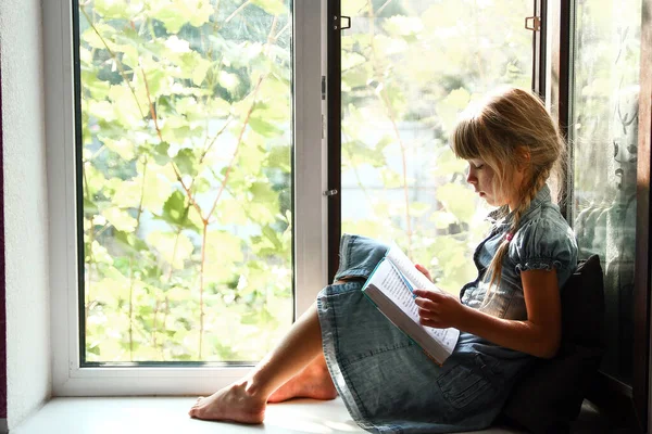 家で窓のそばで本を読んでいる少女 — ストック写真