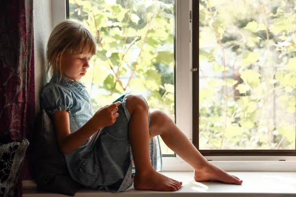 Κοριτσάκι Που Διαβάζει Ένα Βιβλίο Δίπλα Στο Παράθυρο Στο Σπίτι — Φωτογραφία Αρχείου