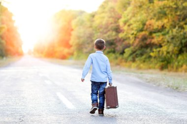 Parka giderken yolda bavulu olan mutlu çocuk.