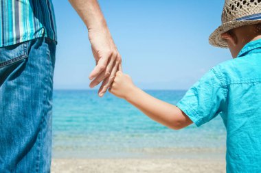 Mutlu bir ebeveynin ve çocuğun elleri doğa yolculuğunda deniz kenarında.