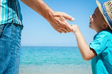 Mutlu bir ebeveynin ve çocuğun elleri doğa yolculuğunda deniz kenarında.