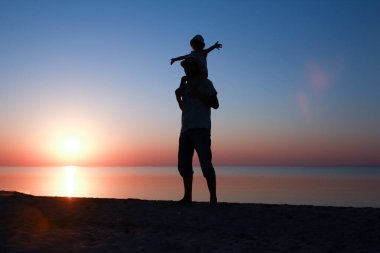 Deniz kenarında çocuklu mutlu bir ebeveyn doğanın silueti üzerinde oynuyor.