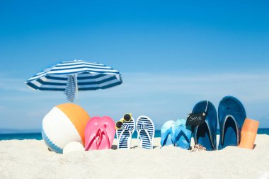 Plaj yaz tatili afişi. Parmak arası terlik ve şapkalı, üzerinde tahta ve top olan okyanus kıyısındaki kumda. Deniz kıyısında yaz aksesuarları. Tropik tatil ve rahat seyahat konsepti. Üst görünüm ve kopyalama alanı.