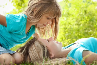 Anne ile çocuk parkta çimlerin üzerinde oynuyorlar.