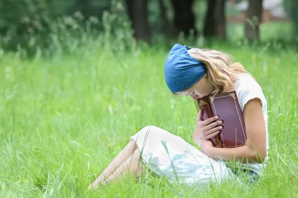 happy girl reading a book on the nature of the Bible in the Park