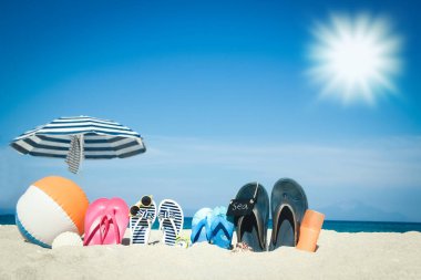 Plaj yaz tatili afişi. Parmak arası terlik ve şapkalı, üzerinde tahta ve top olan okyanus kıyısındaki kumda. Deniz kıyısında yaz aksesuarları. Tropik tatil ve rahat seyahat konsepti. Üst görünüm ve kopyalama alanı.