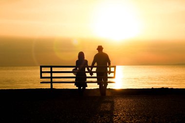 Deniz kenarındaki bankta mutlu bir çift seyahat siluetinde doğanın üzerinde