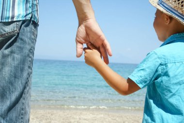 Mutlu bir ebeveynin ve çocuğun elleri doğa yolculuğunda deniz kenarında.
