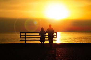 Deniz kenarındaki bankta mutlu bir çift seyahat siluetinde doğanın üzerinde