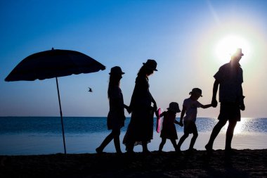 Gün batımında deniz kenarında mutlu bir aile doğada gezici bir siluette