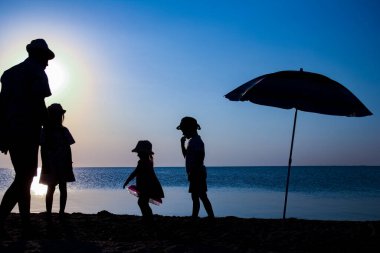 Deniz kenarında çocuklu mutlu bir ebeveyn doğanın silueti üzerinde oynuyor.