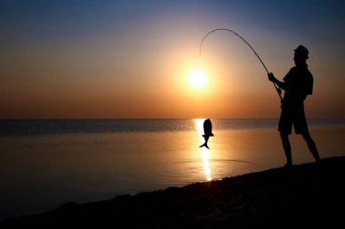 Mutlu balıkçı doğa siluetinde deniz kenarında balık yakalıyor.