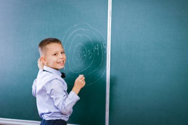 Derste okul tahtasının başında duran mutlu çocuk.