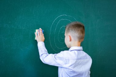 Derste okul tahtasının başında duran mutlu çocuk.