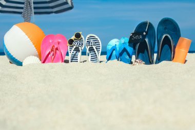 Plaj yaz tatili afişi. Parmak arası terlik ve şapkalı, üzerinde tahta ve top olan okyanus kıyısındaki kumda. Deniz kıyısında yaz aksesuarları. Tropik tatil ve rahat seyahat konsepti. Üst görünüm ve kopyalama alanı.