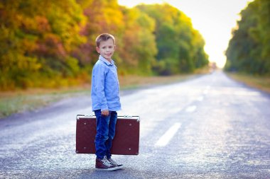 Parka giderken yolda bavulu olan mutlu çocuk.