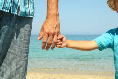 Mutlu bir ebeveynin ve çocuğun elleri doğa yolculuğunda deniz kenarında.