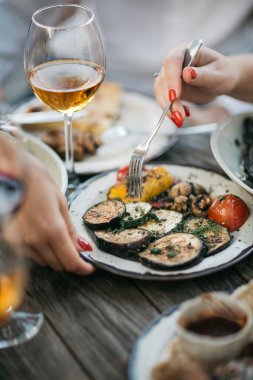 Izgara sebze yiyen insanlar restoran masasında şarapla servis yaparlar. 