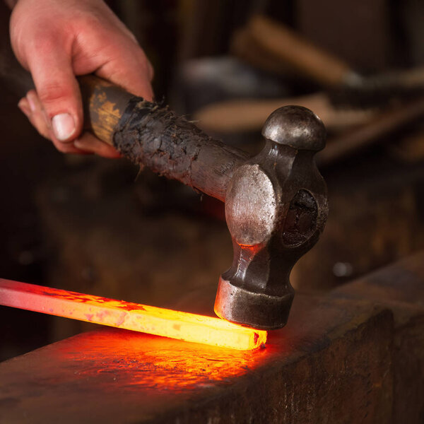 A basic hammer is used to shape red hot steel on an anvil in a forge