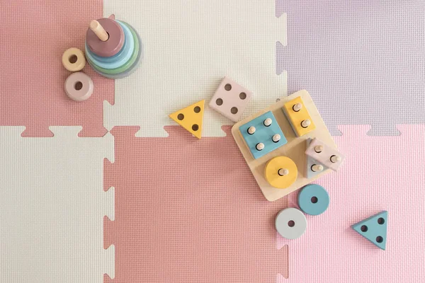 colorful wooden stacking toys on pink play mat in nursery room