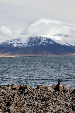 İzlanda 'da karlı dağlarla kıyıdaki istifleme taşı manzarası 