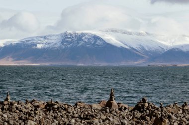 İzlanda 'da karlı dağlarla kıyıdaki istifleme taşı manzarası 