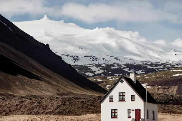 アイスランドの雪山の下の小さなホワイトハウスの風景 ストックフォト