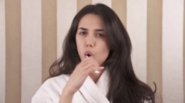 Portrait of a young caucasian woman in a bathrobe cleaning her teeth with a toothbrush