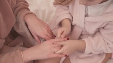A close-up of girl and female's manicured hands, little hands are applying cream and rubbing in into woman's hands massaging them. The woman rubs girl's hands and massages them as well