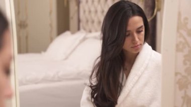 A close up of a charming brunette sitting in front of the mirror. She has a folded cotton sponge and touches her face to finish a makeup foundation. Woman reflection in the mirror.