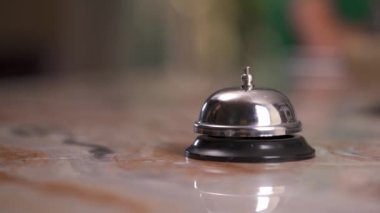 A close up of a bell at the reception desk at the blurred background. Woman's hand moves ahead and presses the button