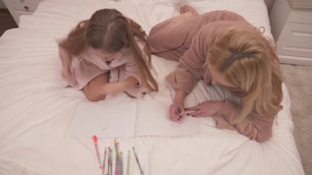 妈妈和女儿穿着长袍躺在床上 继续用彩色钢笔在笔记本上画东西的头像 — 图库视频影像