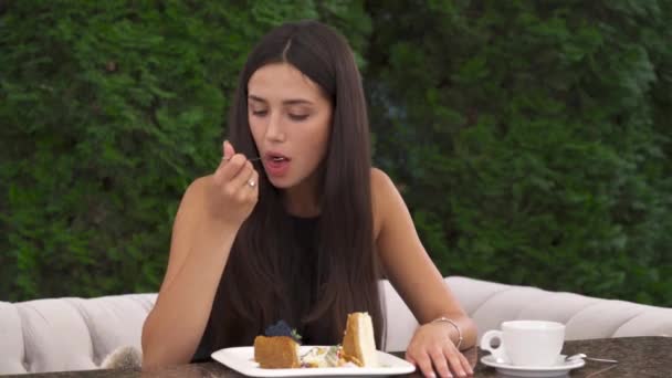 一个漂亮的黑发姑娘在阳台上吃蛋糕的特写镜头 她吃了一块肉 然后摸着她的脸颊 感到牙疼 — 图库视频影像