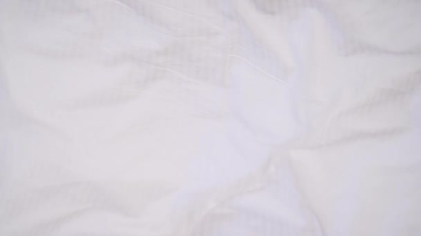 一个年轻的黑发女人的脸的顶部视图 白色的毯子被拿走了 她躺在白色的枕头上 微笑着 调整着头发 移动着肩膀 又藏在毛毯下 — 图库视频影像